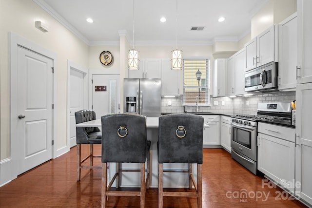 kitchen featuring stainless steel appliances, decorative light fixtures, white cabinets, a breakfast bar, and a center island