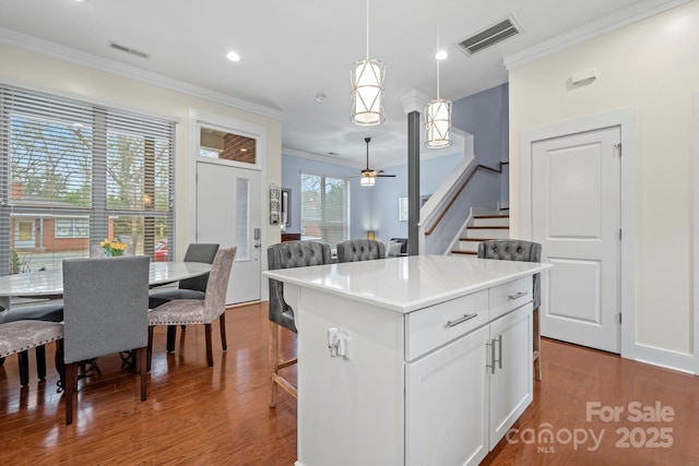 kitchen with pendant lighting, a center island, white cabinetry, ornamental molding, and ceiling fan