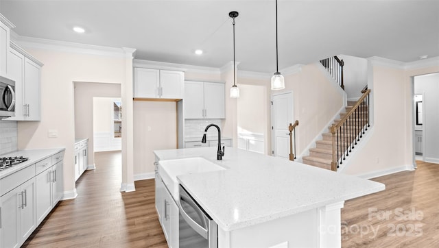 kitchen featuring stainless steel appliances, a kitchen island with sink, backsplash, and hanging light fixtures