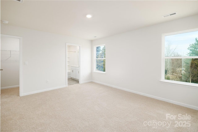 unfurnished bedroom with ensuite bathroom, a closet, a walk in closet, and light carpet