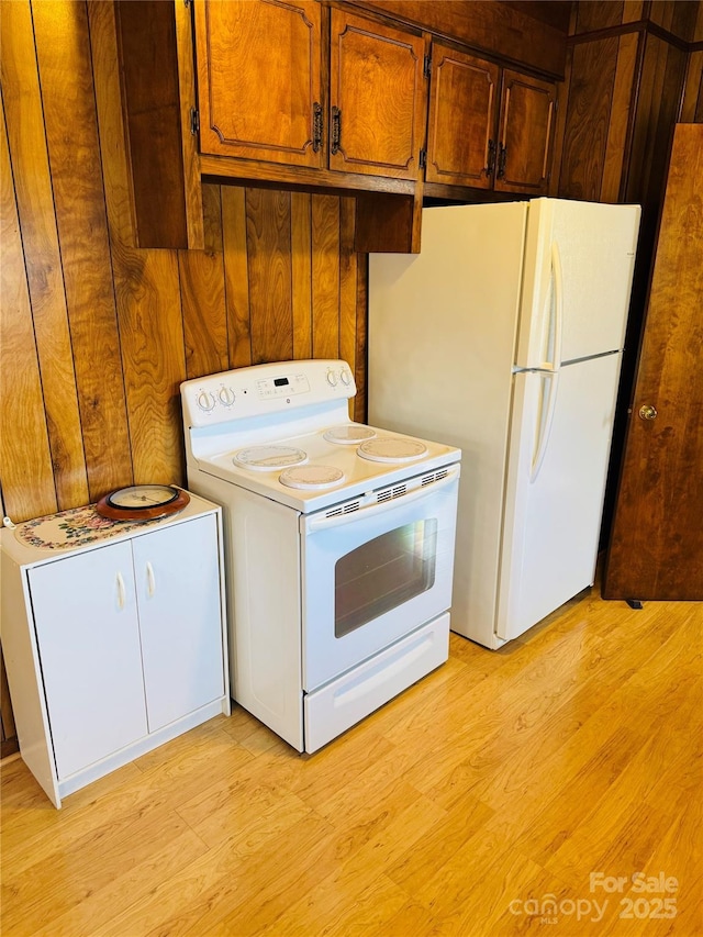 kitchen featuring white appliances, wood walls, and light wood-type flooring