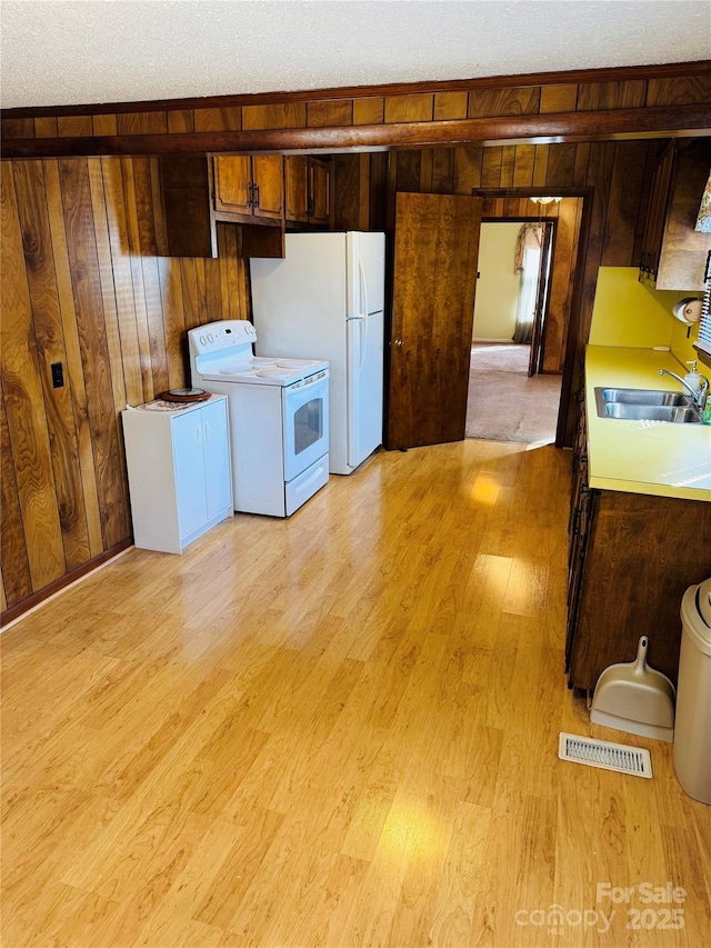 kitchen featuring washer / dryer, white appliances, a textured ceiling, wooden walls, and sink