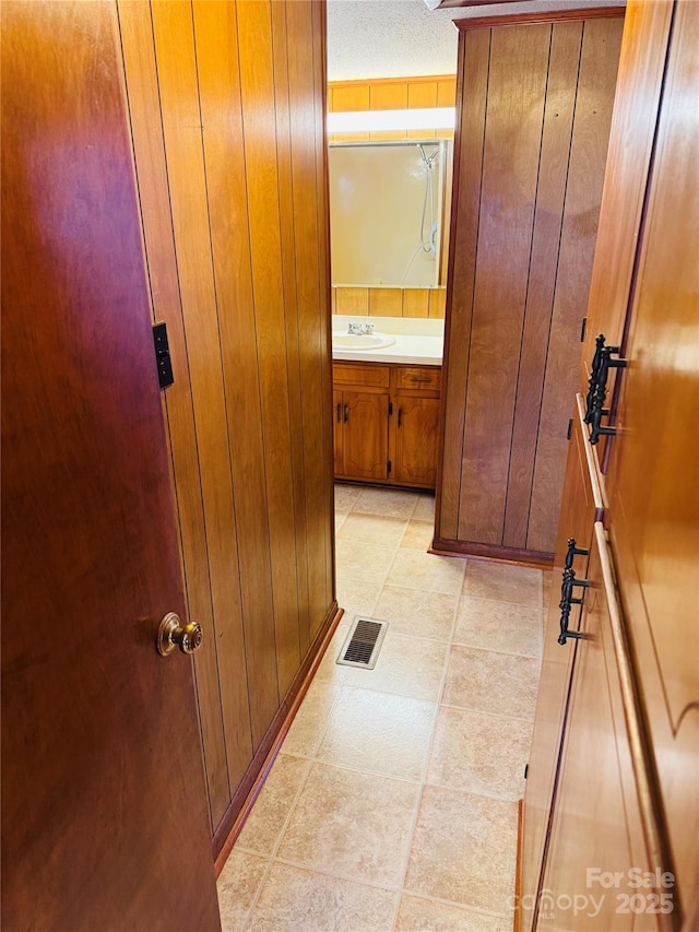 corridor with sink, wooden walls, and a textured ceiling