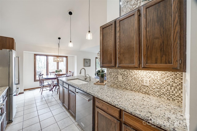 kitchen featuring light stone counters, hanging light fixtures, stainless steel appliances, decorative backsplash, and sink