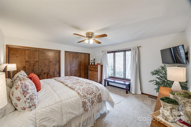 bedroom featuring ceiling fan, light colored carpet, and multiple closets