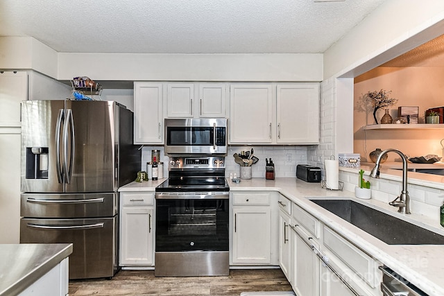 kitchen featuring a textured ceiling, appliances with stainless steel finishes, white cabinets, decorative backsplash, and sink