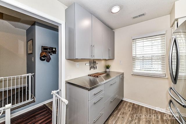 kitchen featuring a textured ceiling, dark hardwood / wood-style floors, gray cabinetry, and stainless steel fridge