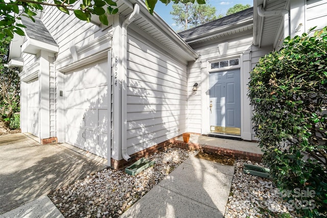 doorway to property featuring an attached garage and a shingled roof