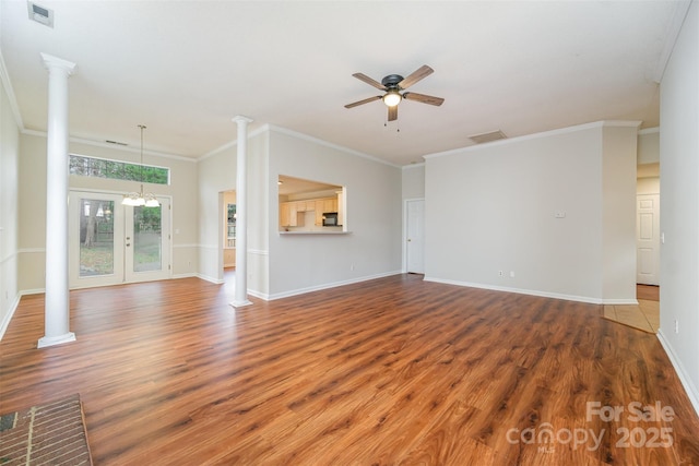 unfurnished living room with visible vents, ceiling fan with notable chandelier, wood finished floors, and ornate columns