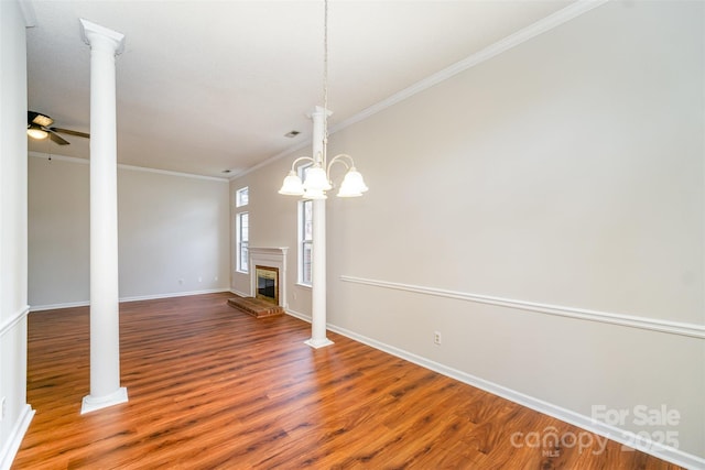 interior space with a glass covered fireplace, wood finished floors, crown molding, decorative columns, and baseboards