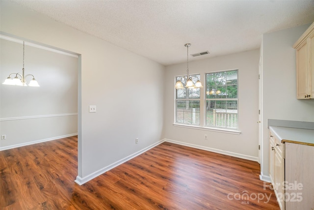 unfurnished dining area featuring a notable chandelier, baseboards, visible vents, and dark wood-style flooring