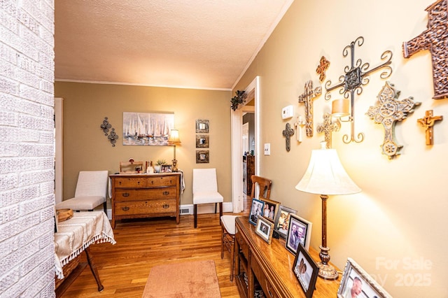 sitting room featuring a textured ceiling, ornamental molding, and light wood-type flooring