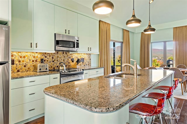 kitchen with appliances with stainless steel finishes, a kitchen island with sink, backsplash, and sink