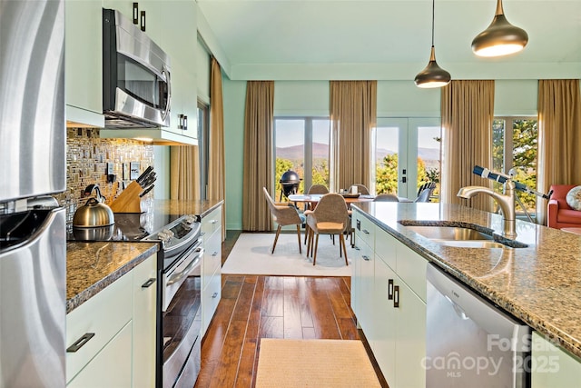 kitchen with appliances with stainless steel finishes, decorative light fixtures, dark stone countertops, white cabinets, and sink