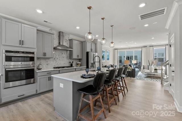 kitchen with a kitchen island with sink, wall chimney exhaust hood, gray cabinetry, and a kitchen breakfast bar