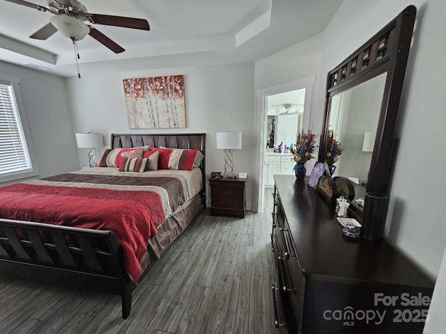 bedroom with connected bathroom, a tray ceiling, hardwood / wood-style floors, and ceiling fan