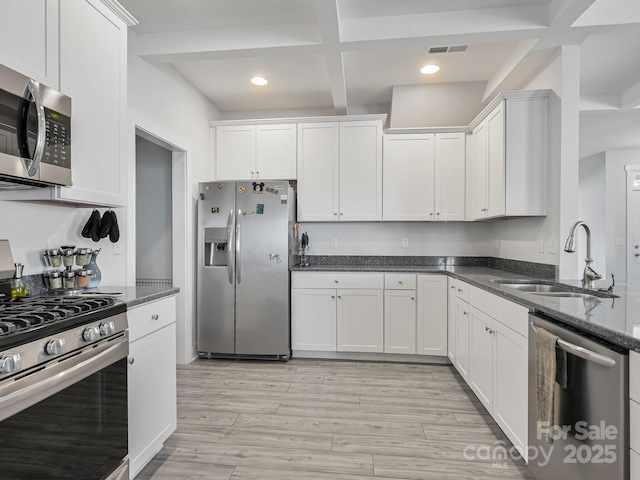 kitchen featuring sink, appliances with stainless steel finishes, white cabinetry, beam ceiling, and dark stone counters