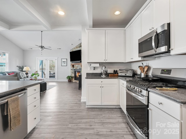 kitchen with a fireplace, white cabinetry, ceiling fan, stainless steel appliances, and light wood-type flooring