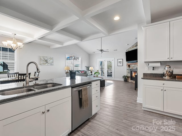 kitchen with sink, ceiling fan with notable chandelier, dishwasher, white cabinetry, and a stone fireplace