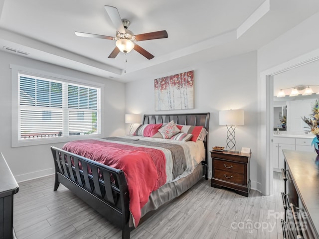 bedroom with a tray ceiling, light hardwood / wood-style flooring, ceiling fan, and ensuite bathroom