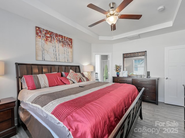 bedroom featuring light hardwood / wood-style flooring, ceiling fan, and a tray ceiling