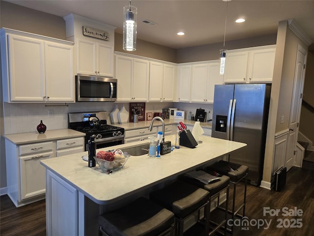 kitchen featuring a kitchen island with sink, white cabinets, pendant lighting, stainless steel appliances, and a breakfast bar area