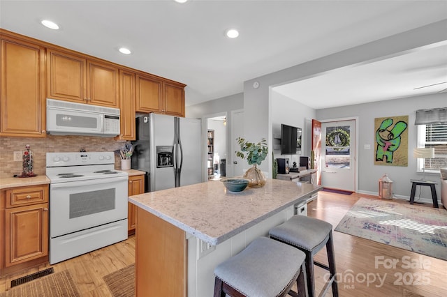 kitchen with white appliances, a kitchen island, a kitchen bar, decorative backsplash, and light wood-type flooring