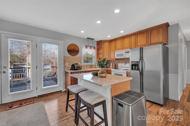 kitchen with stainless steel appliances, a center island, light wood-type flooring, hanging light fixtures, and sink