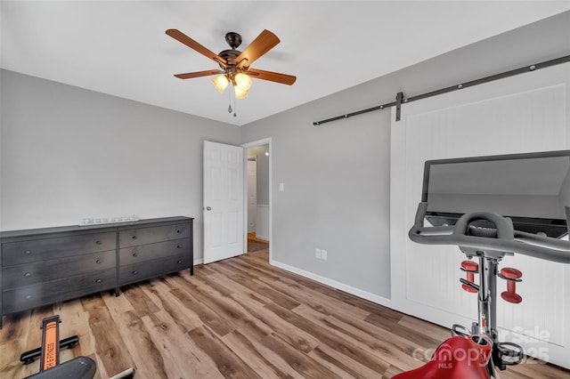 workout room featuring ceiling fan, light hardwood / wood-style floors, and a barn door