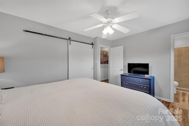 bedroom with ceiling fan, light hardwood / wood-style floors, ensuite bathroom, and a barn door