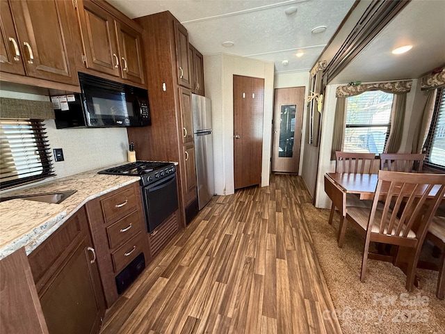 kitchen with light stone countertops, dark hardwood / wood-style flooring, backsplash, and black appliances