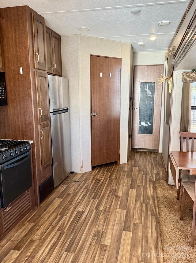 kitchen with black gas stove, dark hardwood / wood-style flooring, and stainless steel refrigerator