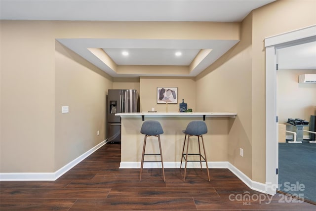 kitchen featuring an AC wall unit, dark hardwood / wood-style floors, stainless steel fridge, a kitchen breakfast bar, and kitchen peninsula