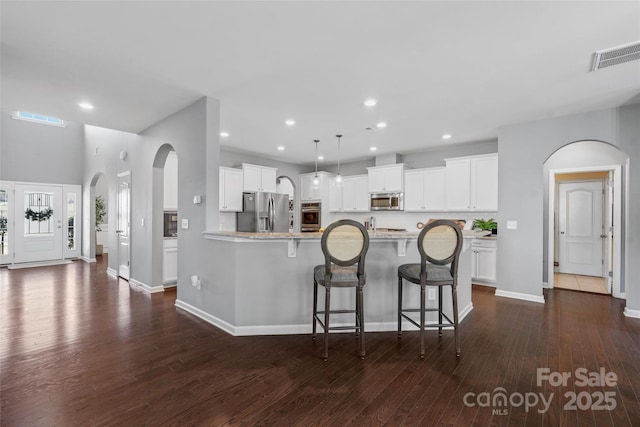 kitchen with a breakfast bar area, white cabinetry, hanging light fixtures, appliances with stainless steel finishes, and light stone countertops