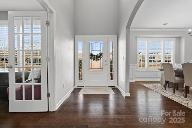 entrance foyer with wood finished floors, a wainscoted wall, arched walkways, ornamental molding, and a decorative wall