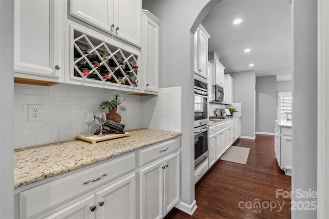 kitchen featuring dark wood finished floors, stainless steel appliances, arched walkways, white cabinets, and light stone countertops