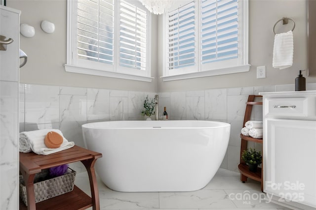 full bath featuring a freestanding tub, marble finish floor, and wainscoting