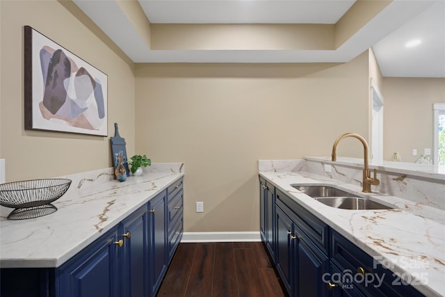 kitchen with blue cabinetry, baseboards, light stone countertops, dark wood finished floors, and a sink