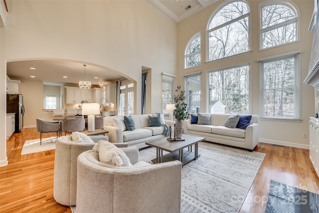 living room with a high ceiling, a healthy amount of sunlight, a notable chandelier, light wood-type flooring, and crown molding