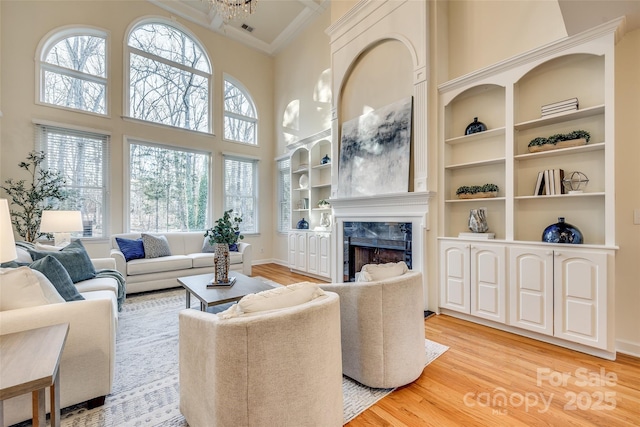 living room featuring an inviting chandelier, a high end fireplace, light hardwood / wood-style floors, and a high ceiling