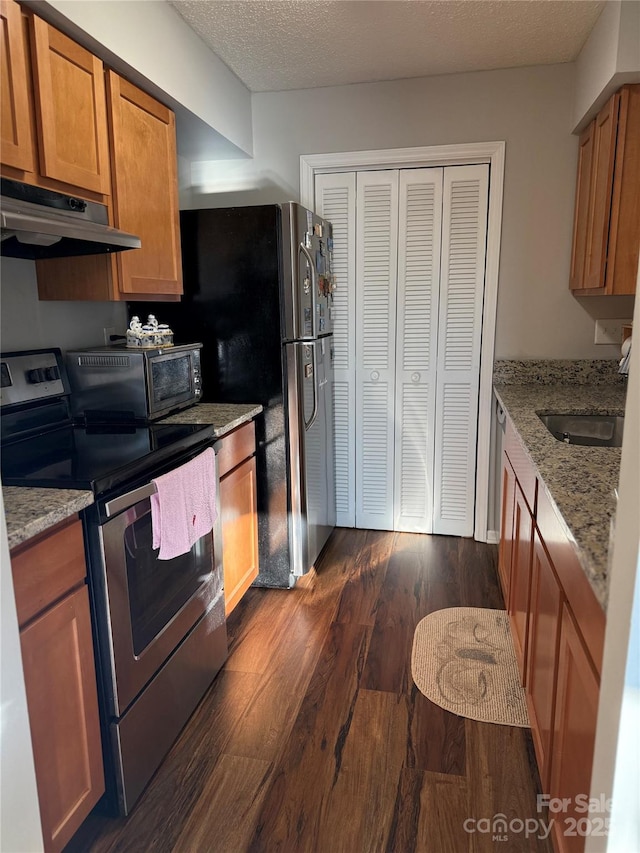 kitchen with stainless steel appliances, dark wood-type flooring, a textured ceiling, light stone counters, and sink