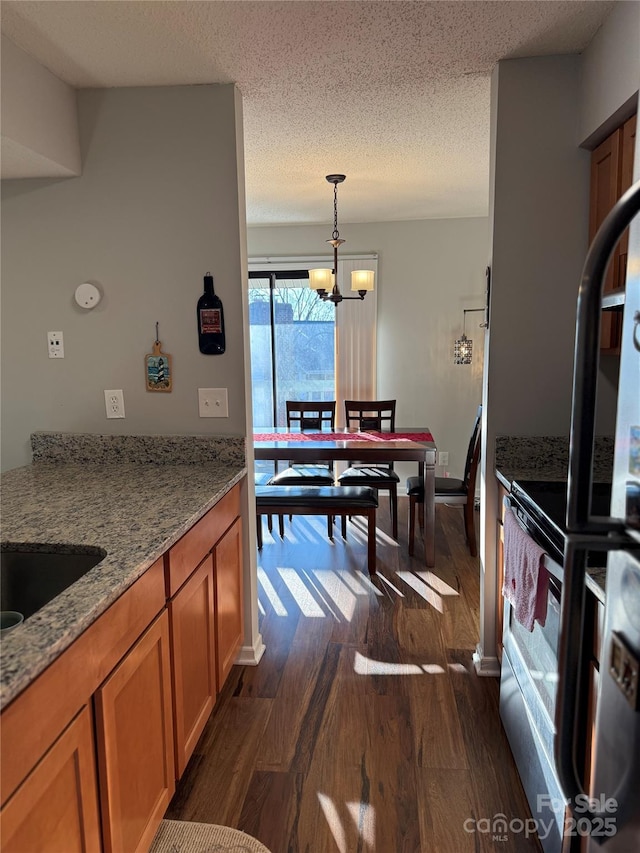 kitchen featuring brown cabinetry, dark wood-style floors, a textured ceiling, and light stone countertops