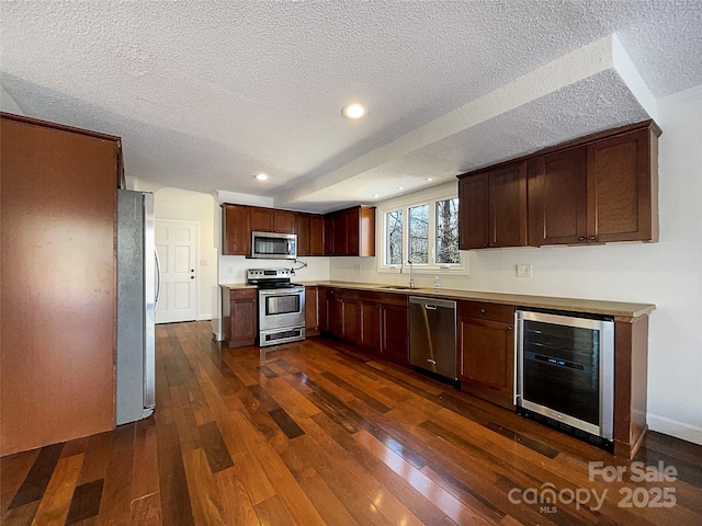 kitchen with wine cooler, sink, appliances with stainless steel finishes, dark wood-type flooring, and a textured ceiling