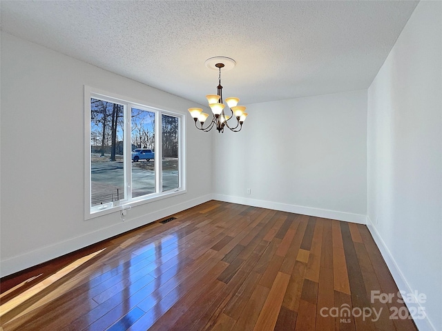 unfurnished dining area with a textured ceiling, dark hardwood / wood-style floors, and an inviting chandelier