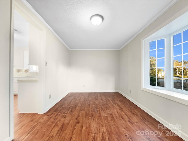 empty room featuring a textured ceiling, light wood-type flooring, and ornamental molding