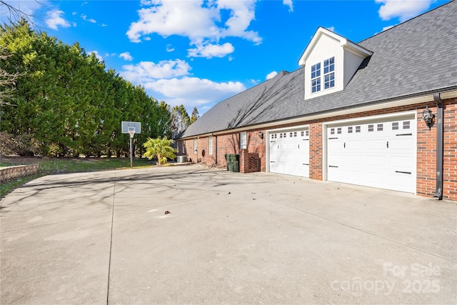 view of side of property featuring a garage, brick siding, driveway, and a shingled roof