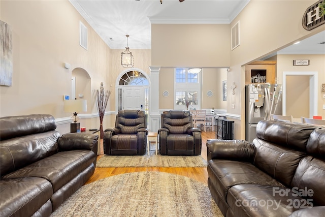 living area with light wood-type flooring, visible vents, and crown molding