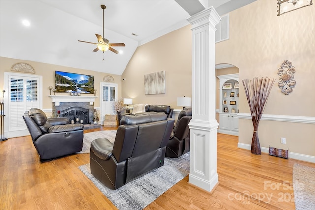 living area with high vaulted ceiling, light wood-style floors, a fireplace, ceiling fan, and ornate columns