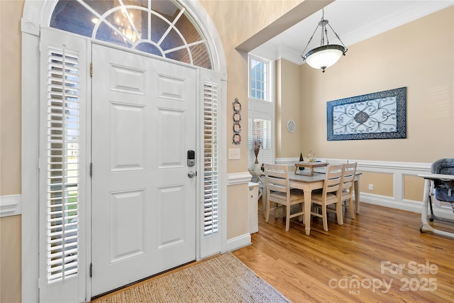 foyer entrance with a wainscoted wall, a decorative wall, ornamental molding, and light wood finished floors