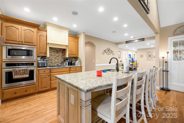 kitchen featuring a sink, light stone counters, tasteful backsplash, arched walkways, and appliances with stainless steel finishes